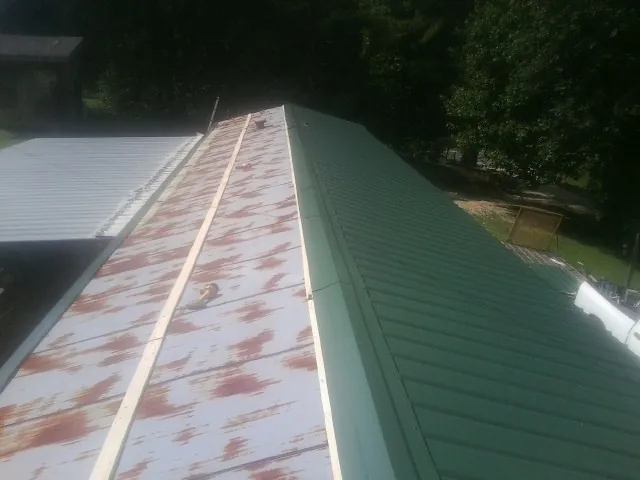 Old rusted panels beside newly installed green metal roofing — Wind Damage Roof Repair by Roofing Brothers in Midland