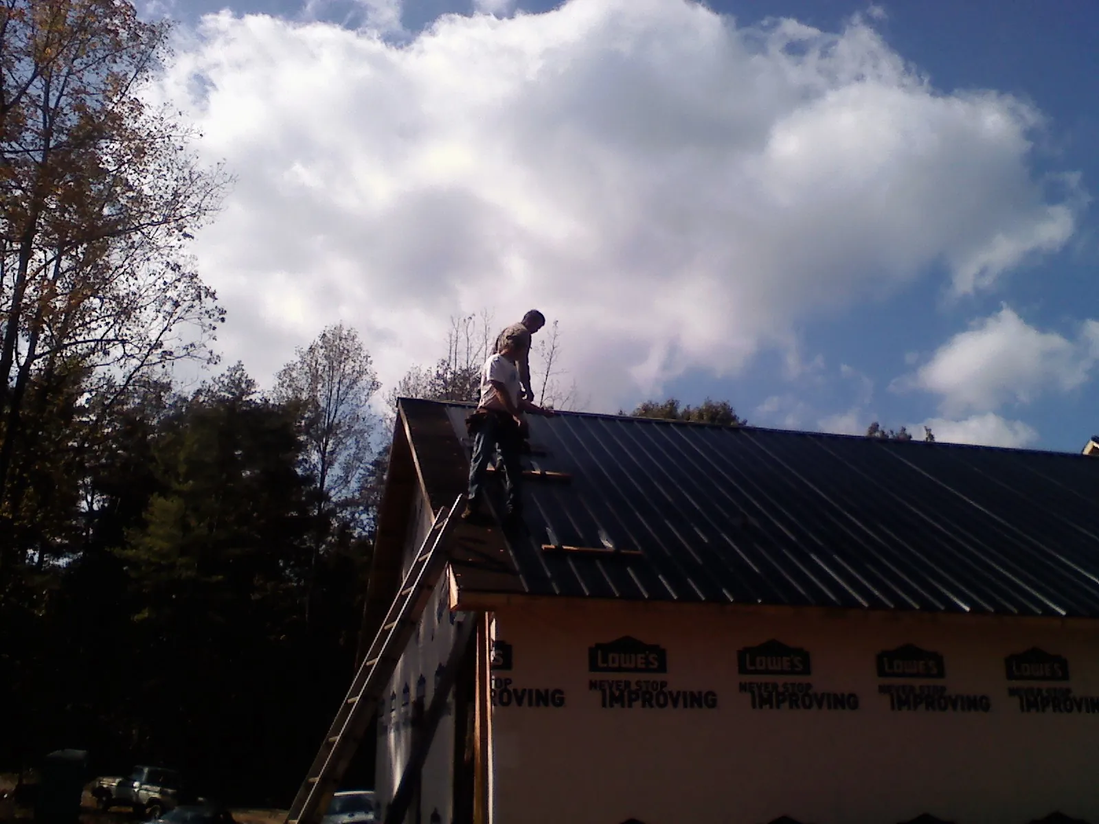 Roofer fastening dark metal panels high against a cloudy sky, from a Roof Inspection job in Midland